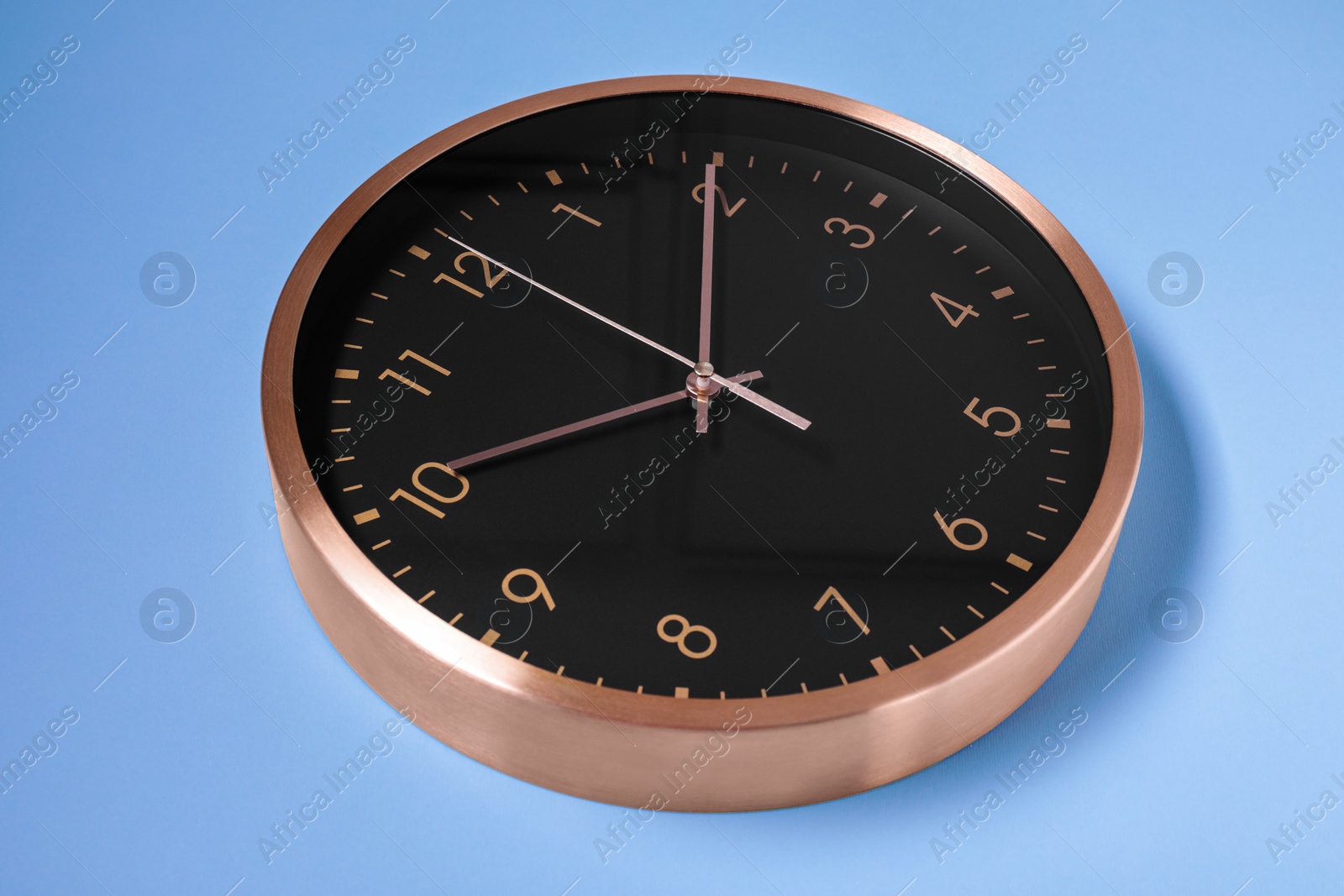 Photo of Stylish round clock on light blue background, closeup. Interior element