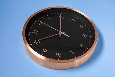 Stylish round clock on light blue background, closeup. Interior element