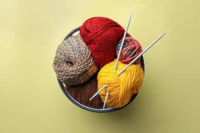 Photo of Soft woolen yarns and knitting needles on yellow background, top view