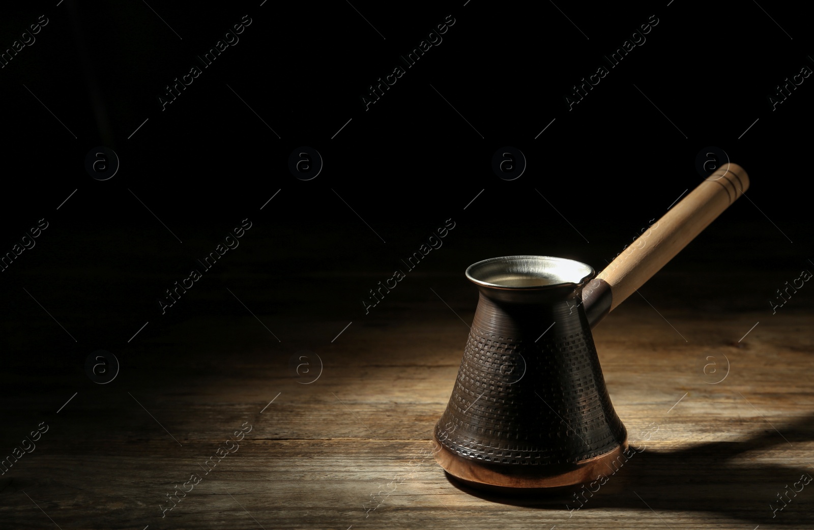 Photo of Beautiful copper turkish coffee pot on wooden table against dark background, space for text