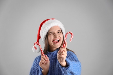 Photo of Playful woman in Santa hat and blue sweater holding candy canes on grey background