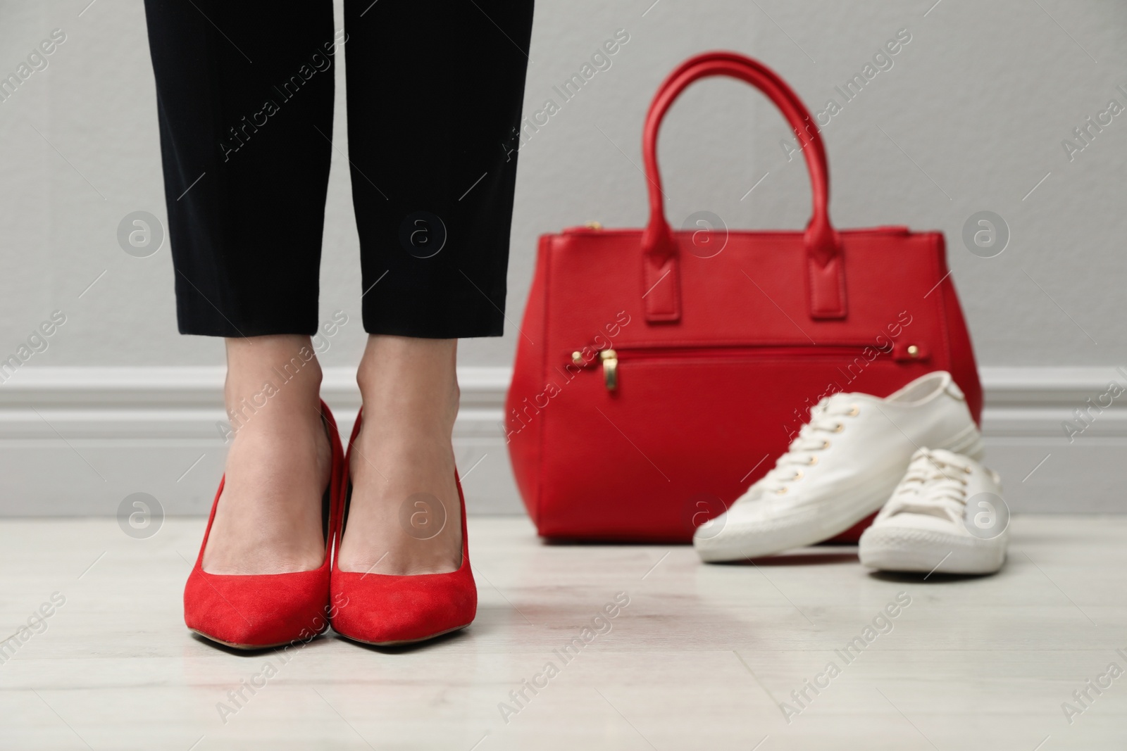 Photo of Businesswoman in high heel shoes standing near comfortable sneakers and bag indoors, closeup