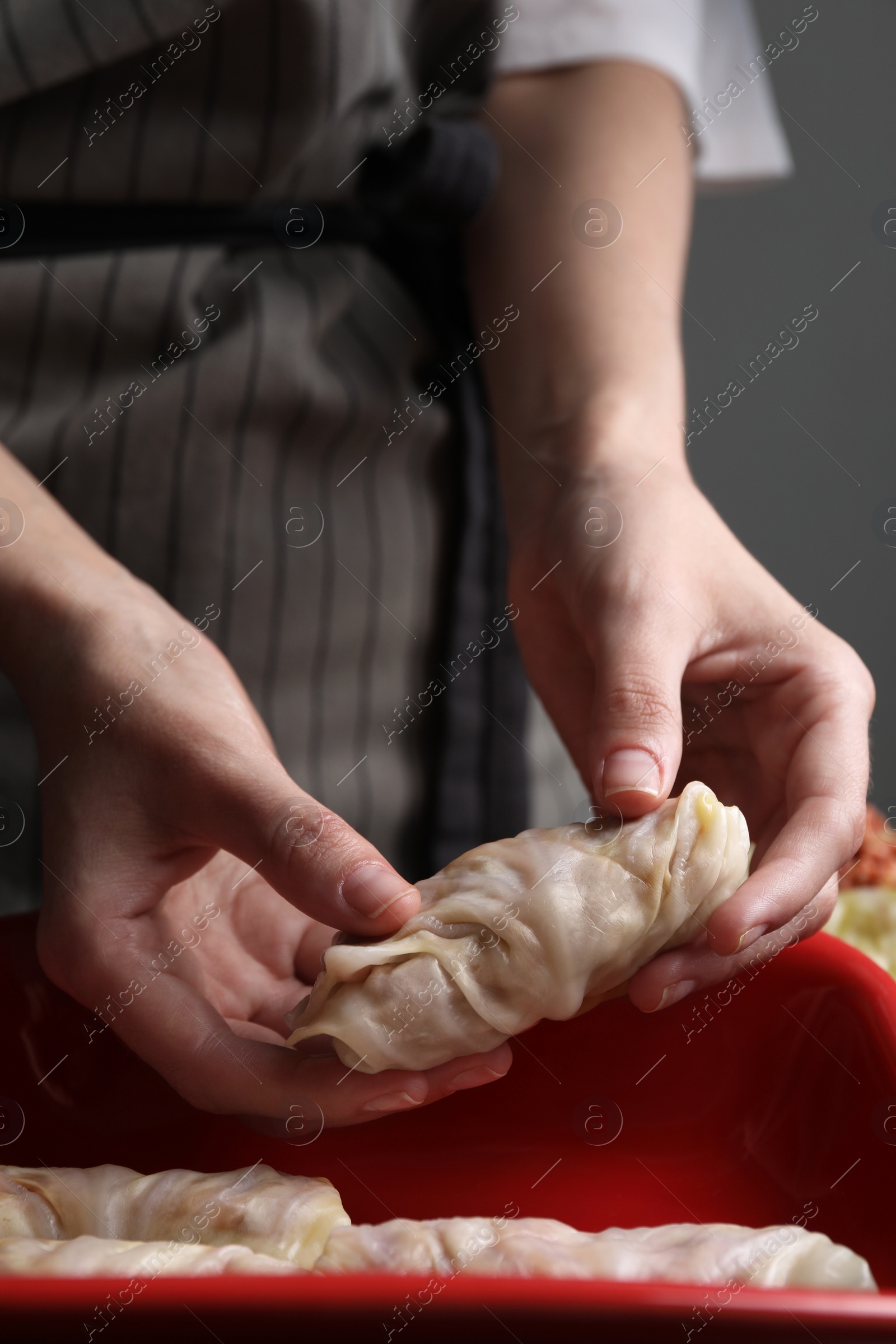 Photo of Woman putting uncooked stuffed cabbage roll into baking dish at table, closeup