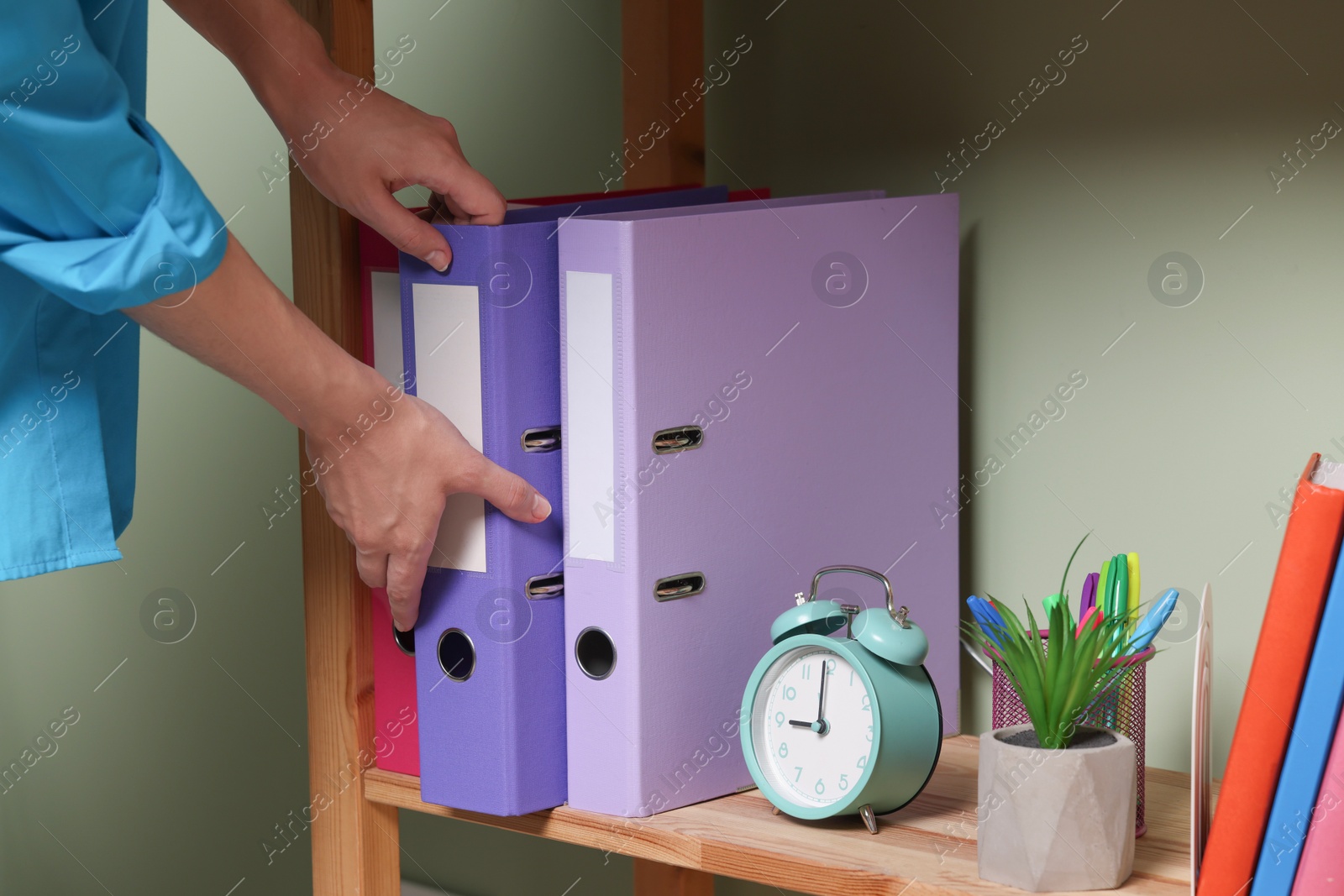 Photo of Woman taking binder office folder from shelving unit indoors, closeup