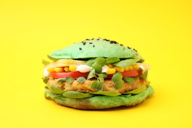 Photo of Tasty green vegan burger with vegetables, patty and microgreens on yellow background, closeup