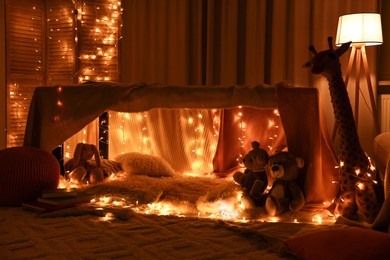 Beautiful play tent decorated with festive lights and toys at home
