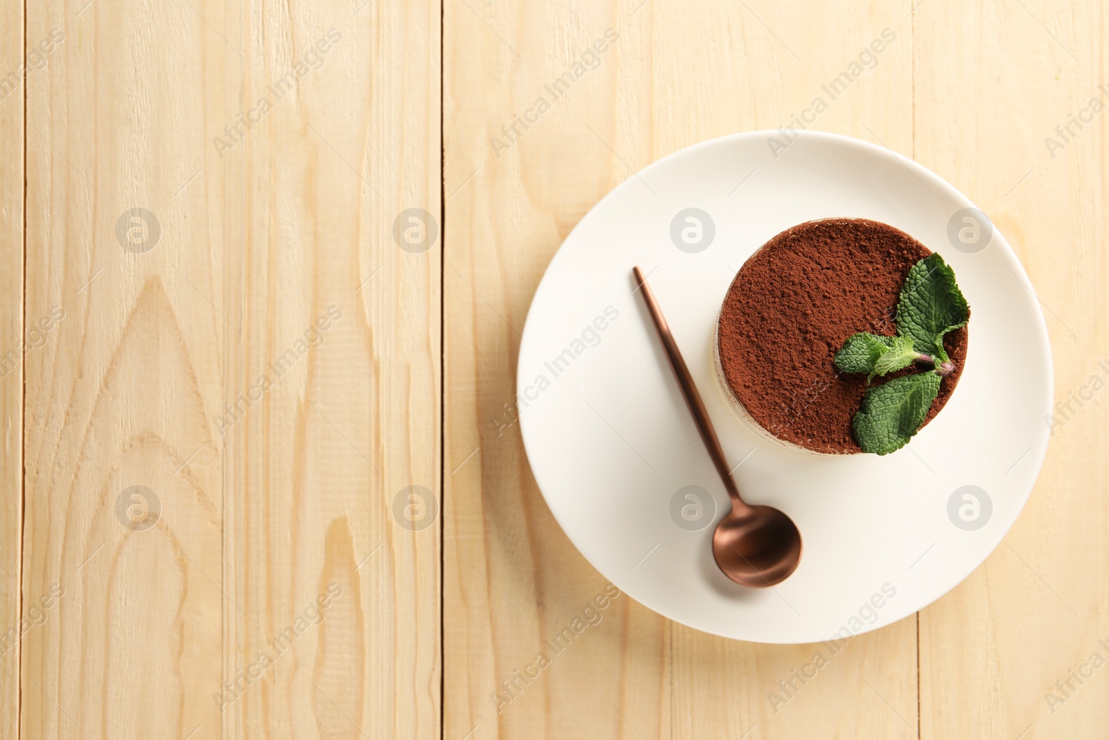 Photo of Tasty tiramisu and mint in glass on light wooden table, top view. Space for text