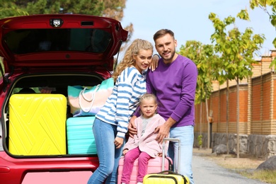 Happy young family with suitcases standing near car outdoors