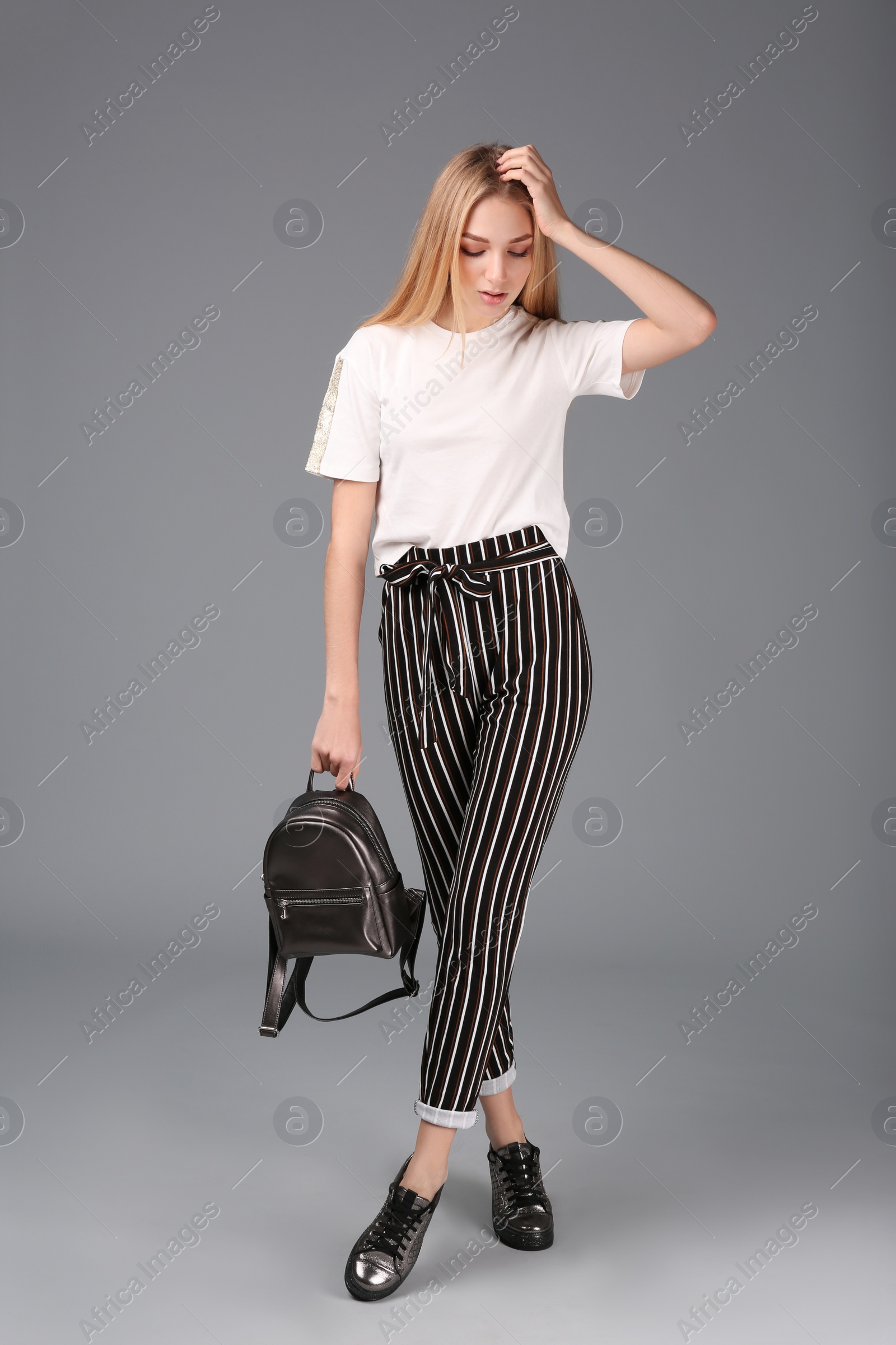 Photo of Young stylish woman in trendy sport shoes with backpack on grey background