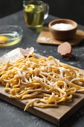 Photo of Board with homemade pasta and ingredients on dark table