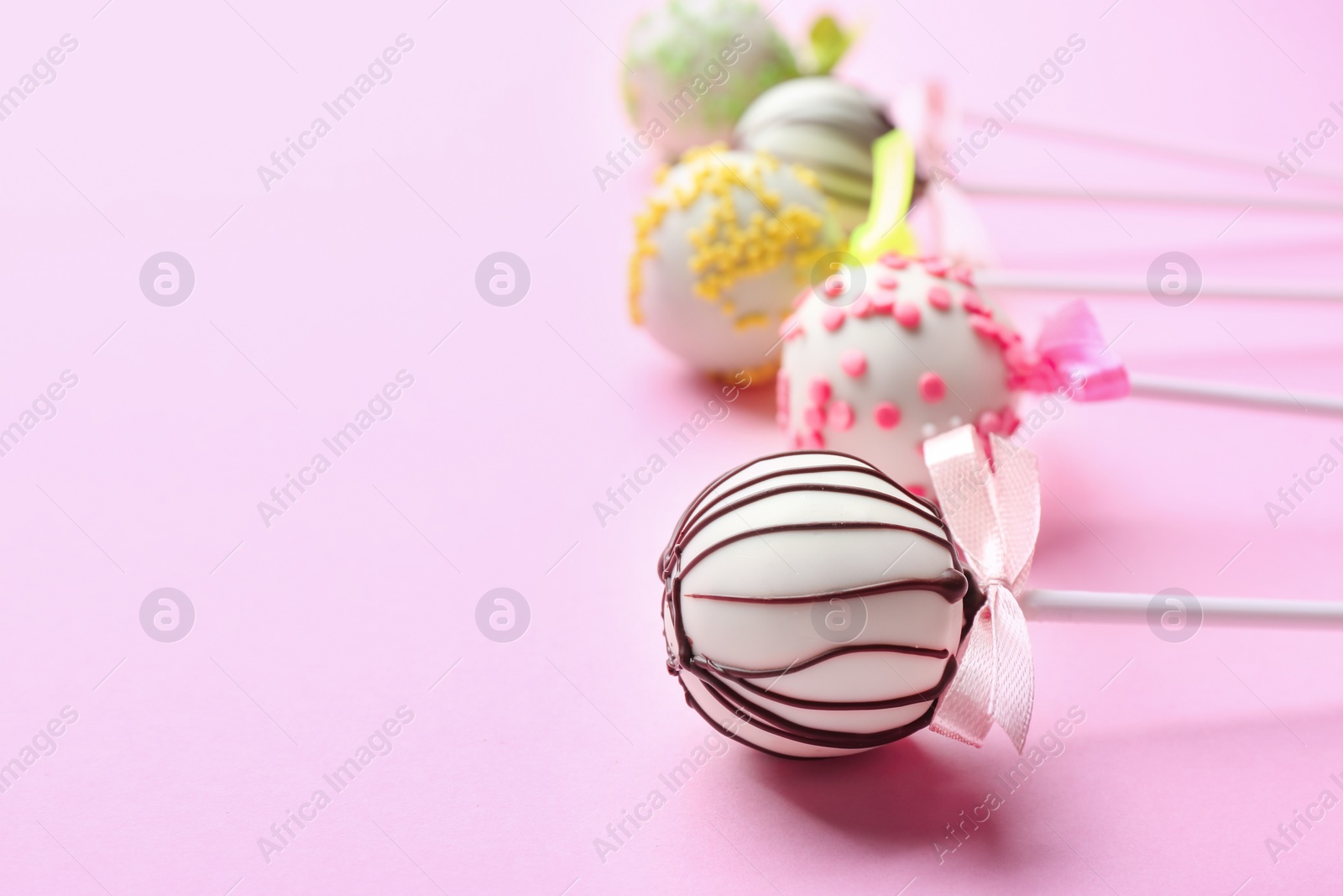 Photo of Different tasty cake pops on light pink background. Space for text