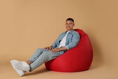 Photo of Happy man on red bean bag chair against beige background