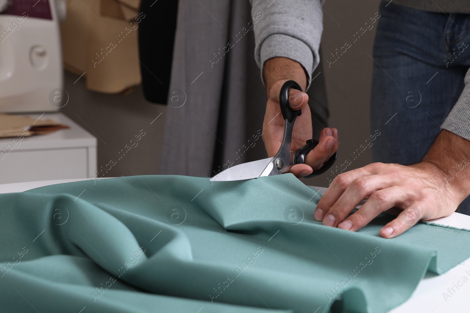 Photo of Tailor cutting fabric with scissors at table in atelier, closeup