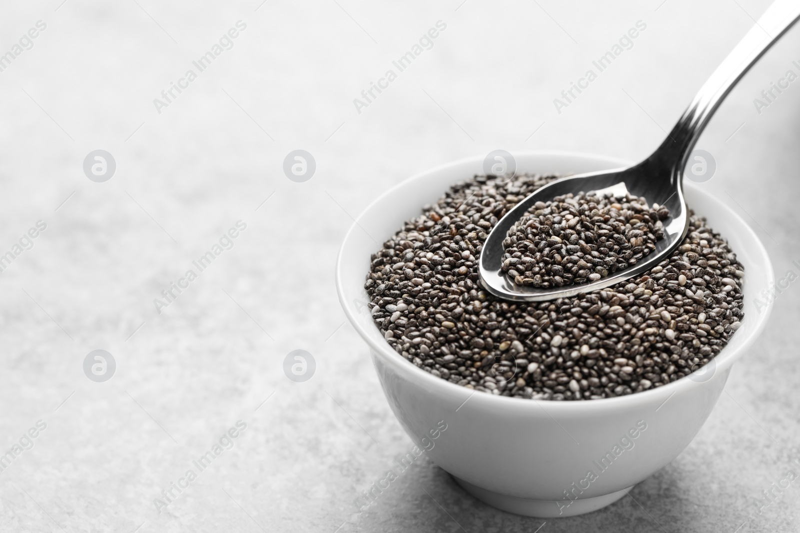 Photo of Bowl and spoon with chia seeds on grey table, space for text