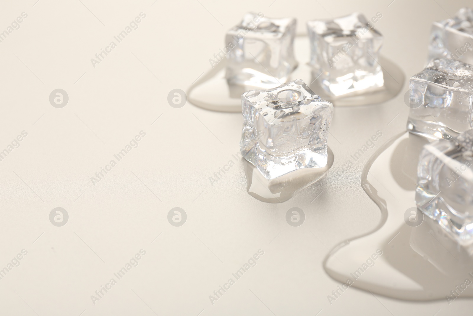 Photo of Melting ice cubes and water drops on light grey background, closeup. Space for text