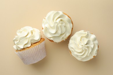 Photo of Tasty vanilla cupcakes with cream on beige background, top view