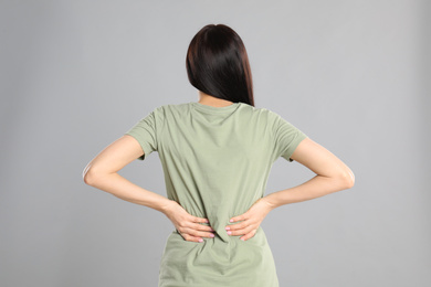 Photo of Woman suffering from lower back pain on light grey background. Visiting orthopedist