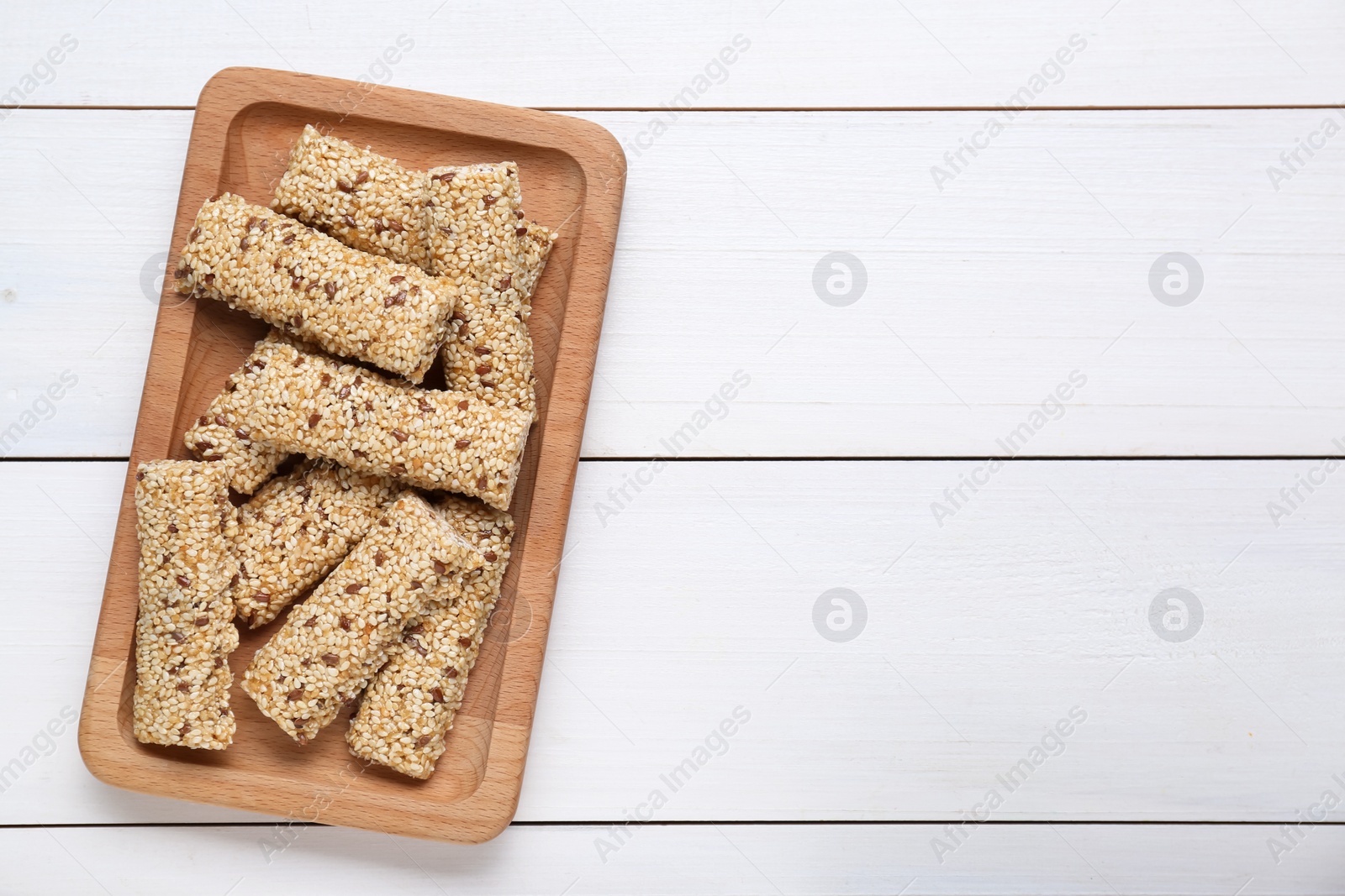 Photo of Plate with tasty sesame seed bars on white wooden table, top view. Space for text