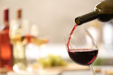 Pouring red wine from bottle into glass on blurred background. Space for text