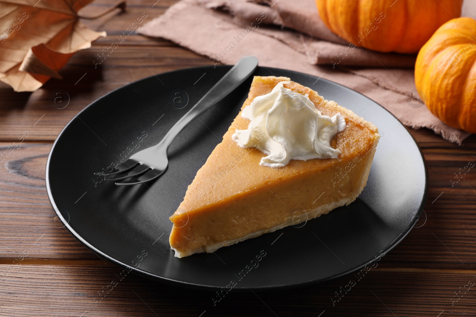 Photo of Piece of delicious pumpkin pie with whipped cream and fork on wooden table, closeup