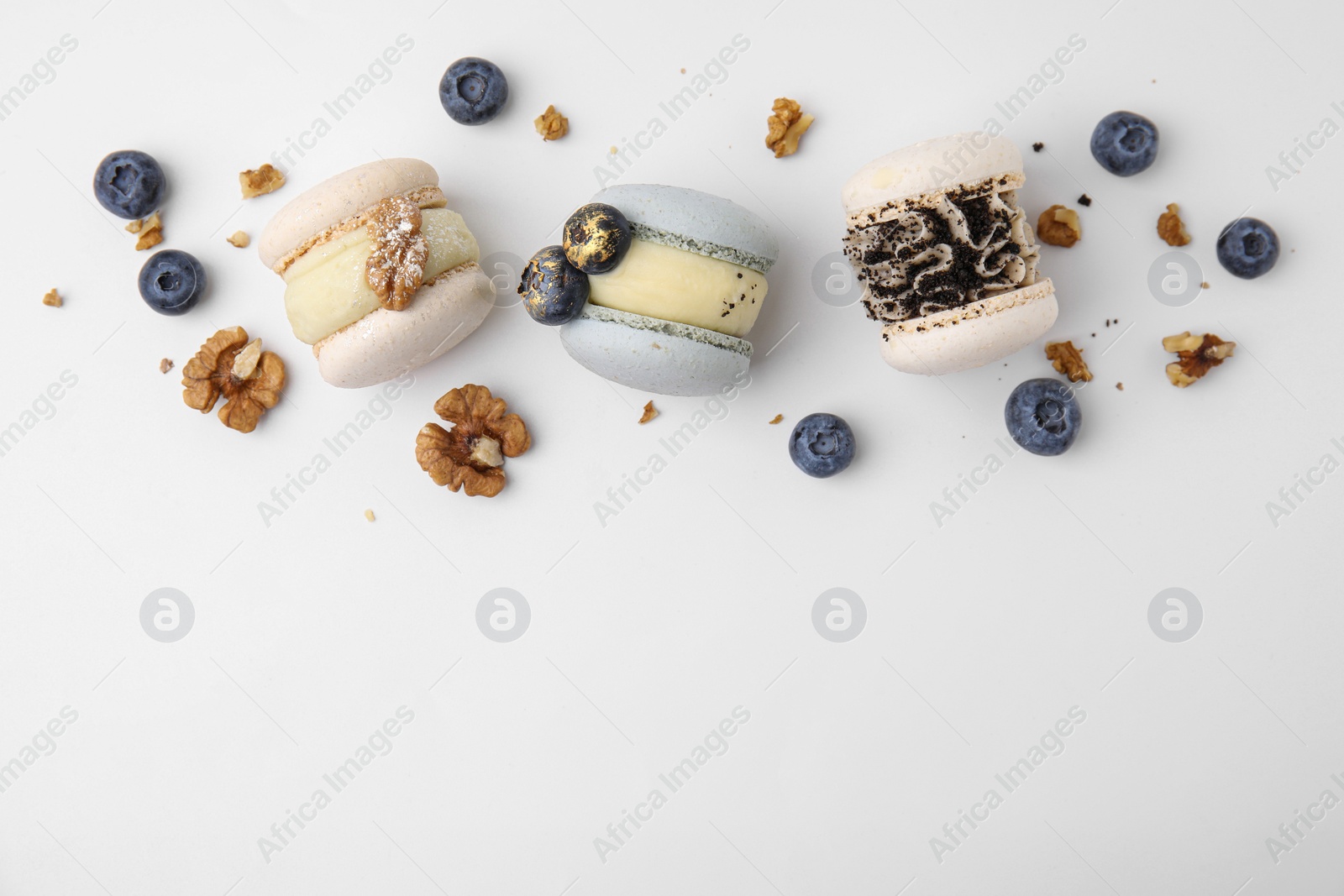 Photo of Delicious macarons, walnuts and blueberries on white table, flat lay. Space for text