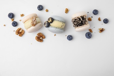 Delicious macarons, walnuts and blueberries on white table, flat lay. Space for text