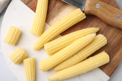 Photo of Tasty fresh yellow baby corns and knife on tray, top view