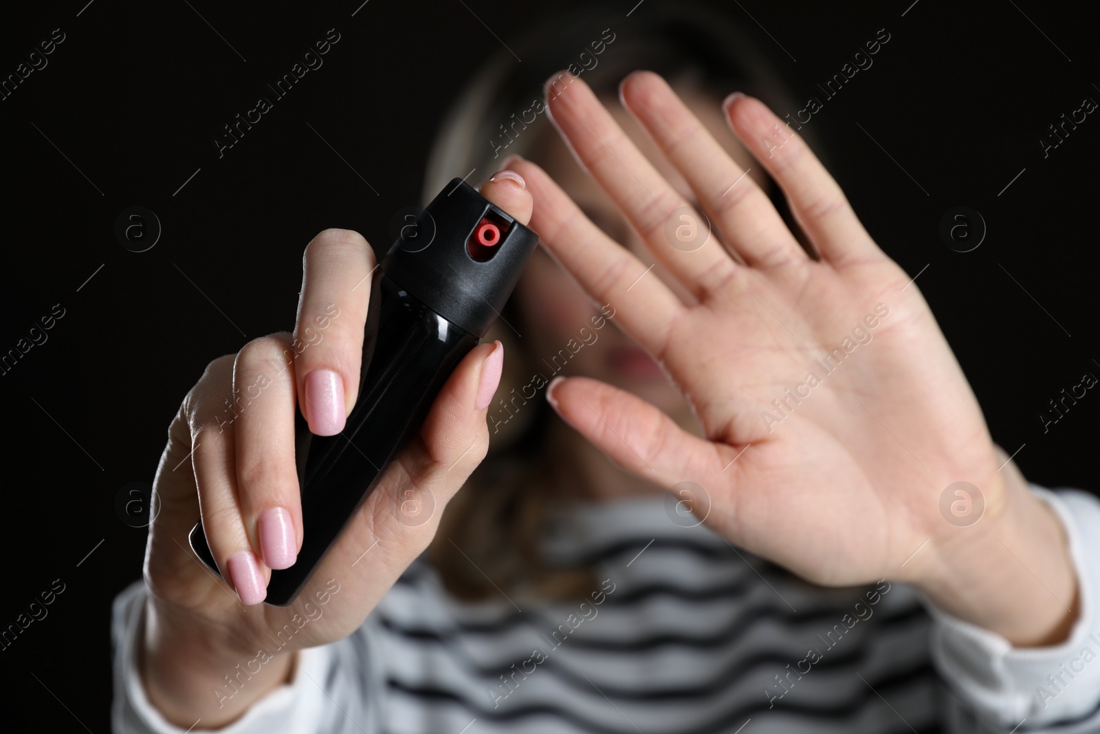 Photo of Young woman using pepper spray against black background, focus on hands