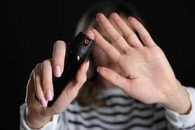 Photo of Young woman using pepper spray against black background, focus on hands