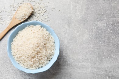 Photo of Raw basmati rice in bowl and spoon on grey table, top view. Space for text