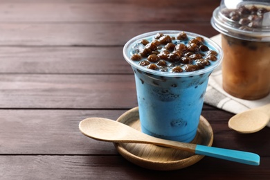 Tasty blue milk bubble tea and spoon on brown wooden table, closeup. Space for text