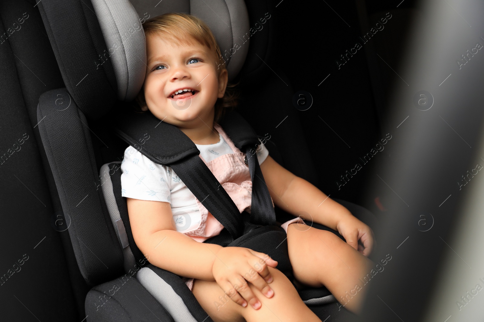 Photo of Cute little girl sitting in child safety seat inside car