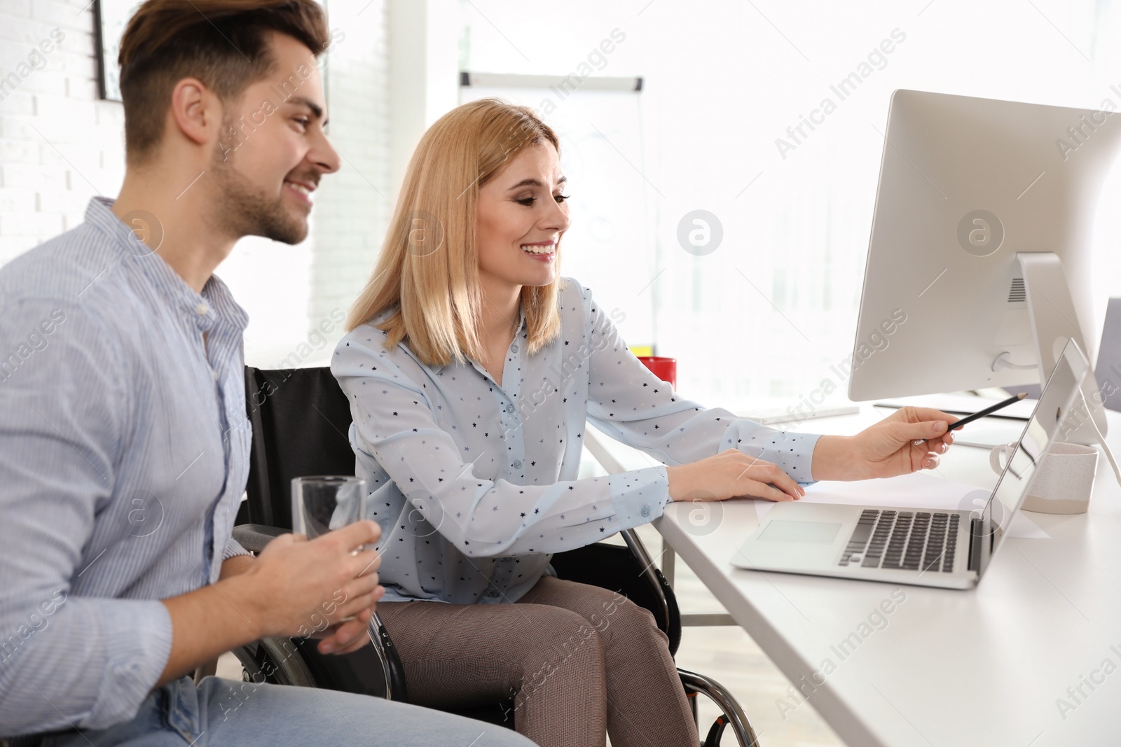 Photo of Woman in wheelchair with her colleague at workplace