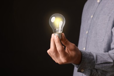 Photo of Glow up your ideas. Closeup view of man holding light bulb on black background, space for text