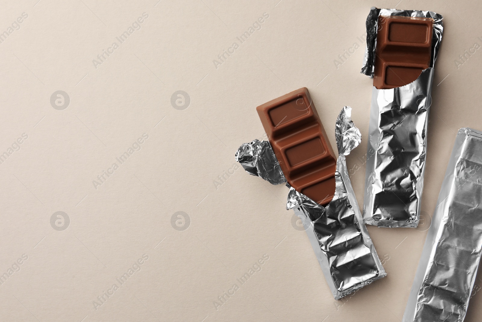 Photo of Tasty chocolate bars wrapped in foil on light background, flat lay. Space for text