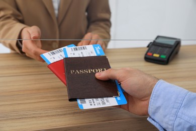 Photo of Man giving passports with tickets to agent at check-in desk in airport, closeup