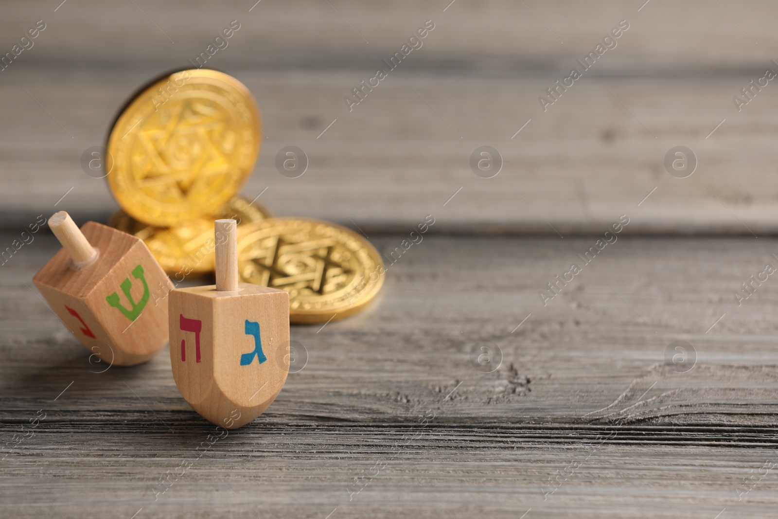 Photo of Dreidels with Jewish letters and coins on wooden table, space for text. Traditional Hanukkah game