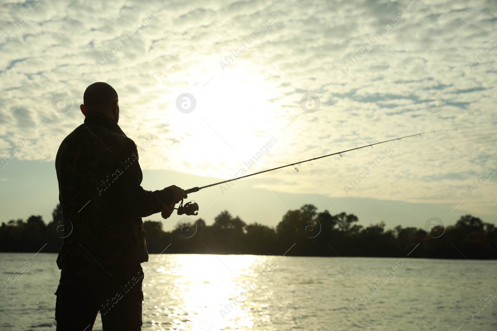 Photo of Fisherman with rod fishing at riverside, back view