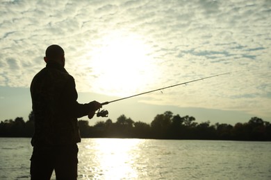 Photo of Fisherman with rod fishing at riverside, back view