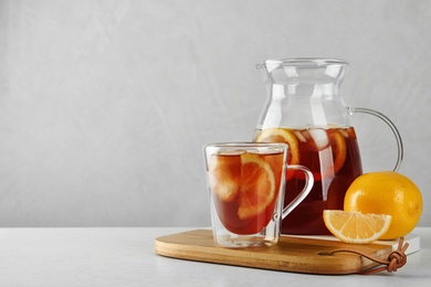 Cup and jug of refreshing iced tea on white table against light background. Space for text