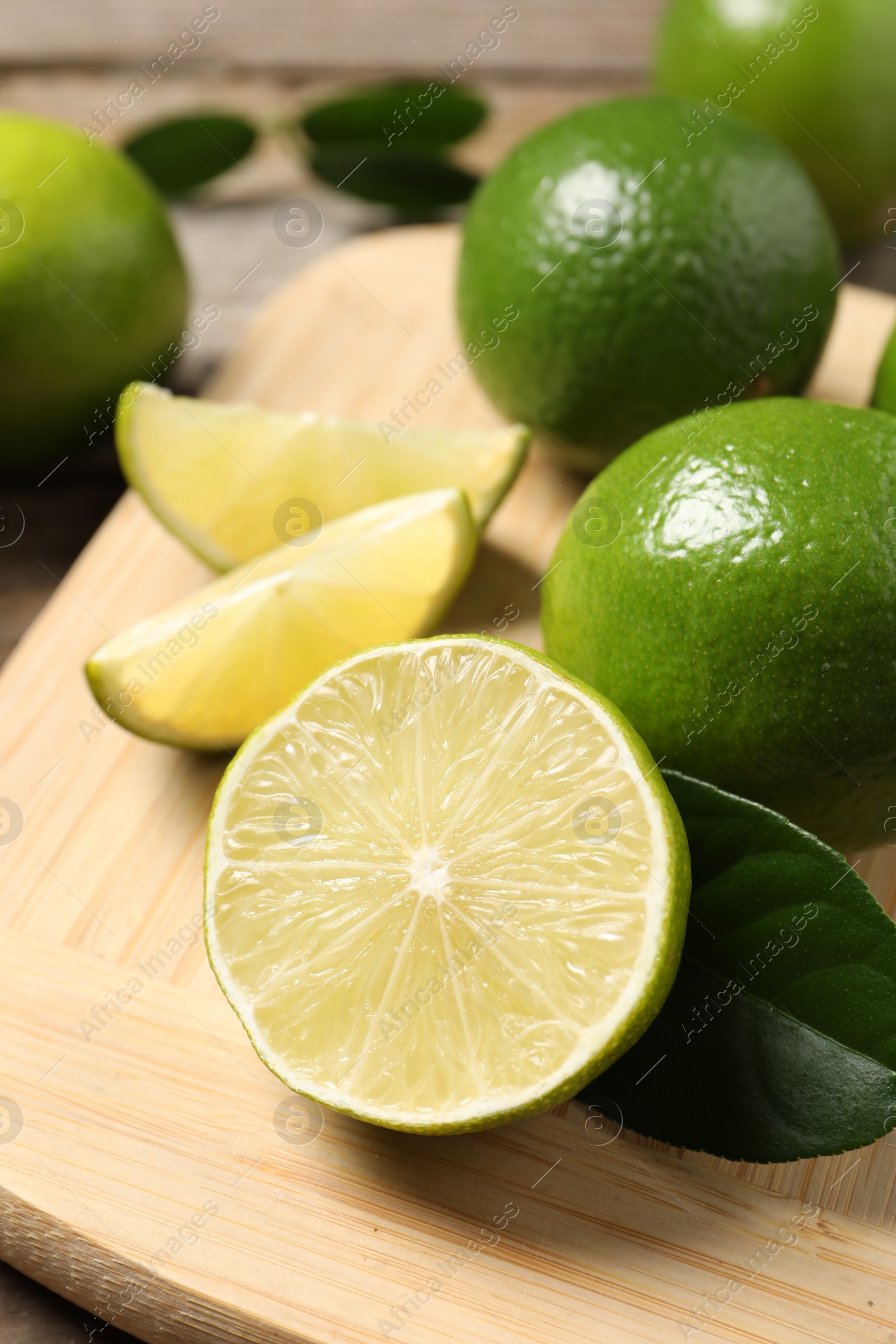 Photo of Whole and cut fresh limes on wooden board, closeup