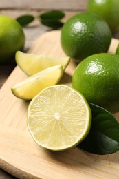 Whole and cut fresh limes on wooden board, closeup