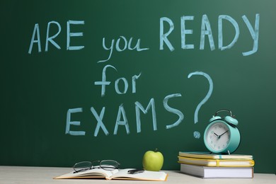 Different stationery and alarm clock on wooden table near chalkboard with phrase Are You Ready For Exams