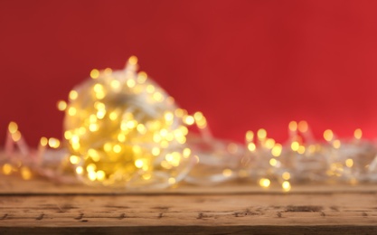 Photo of Yellow Christmas lights on wooden table against red background, blurred view