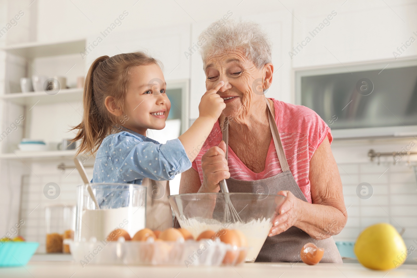 Photo of Cute girl and her grandmother cooking in kitchen