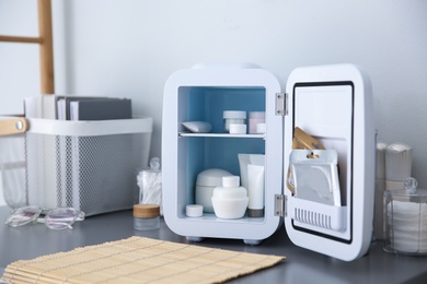 Photo of Mini fridge with cosmetic products on grey vanity table indoors