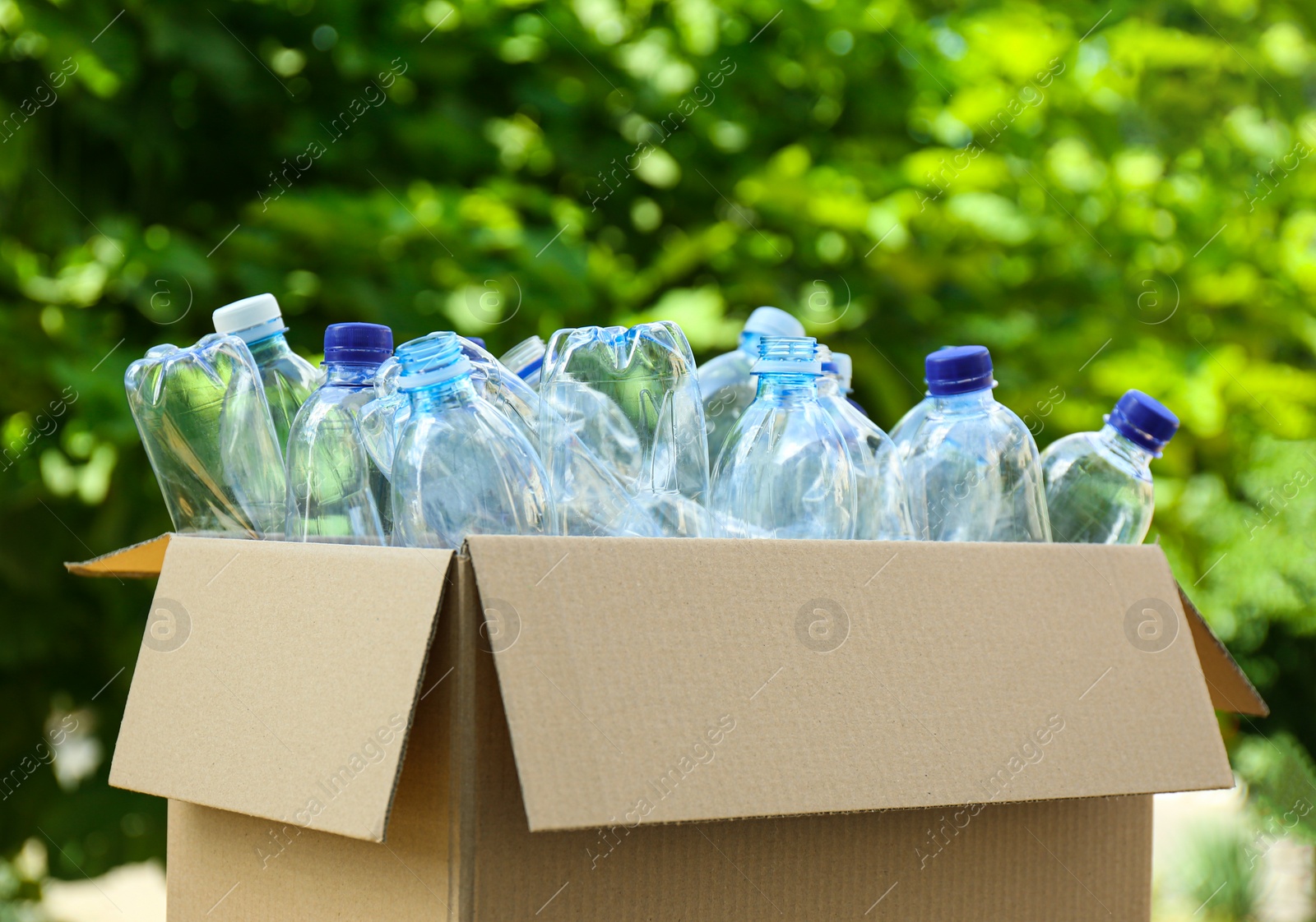 Photo of Cardboard box with used plastic bottles outdoors. Recycle concept