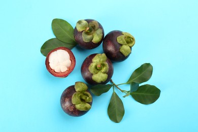 Photo of Fresh ripe mangosteen fruits with green leaves on turquoise background, flat lay