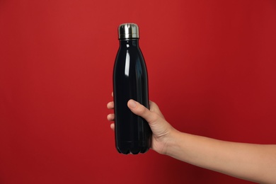 Photo of Woman holding modern dark thermos on red background, closeup