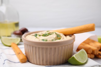 Delicious hummus with grissini sticks, lime and olives on light table
